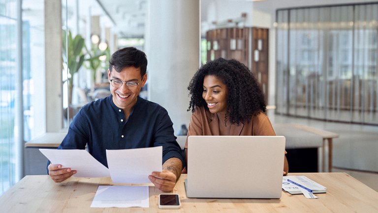 Zwei Personen analysieren gemeinsam Finanzunterlagen am Laptop.