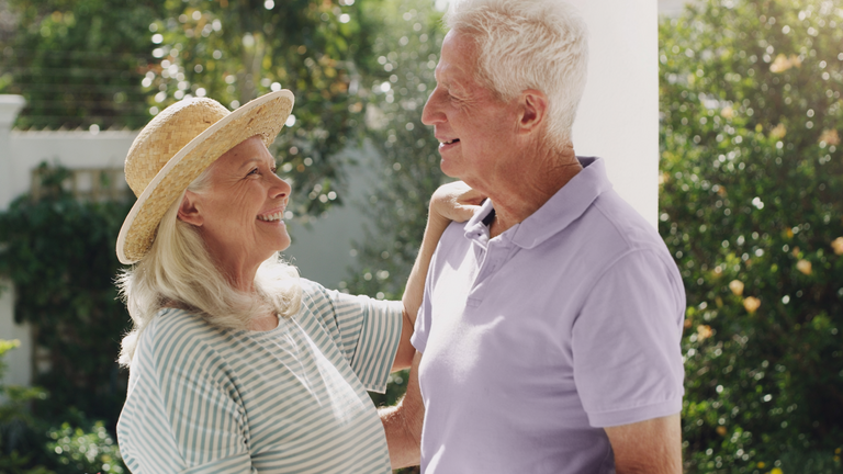 Älteres Paar lächelt sich im Garten liebevoll an.