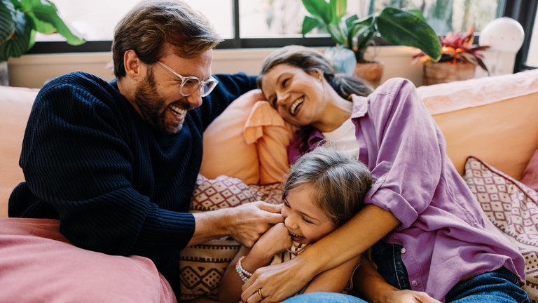 Familie kuschelt lachend auf dem Sofa.