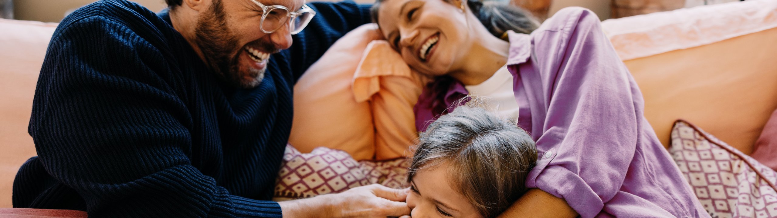 Familie kuschelt lachend auf dem Sofa.