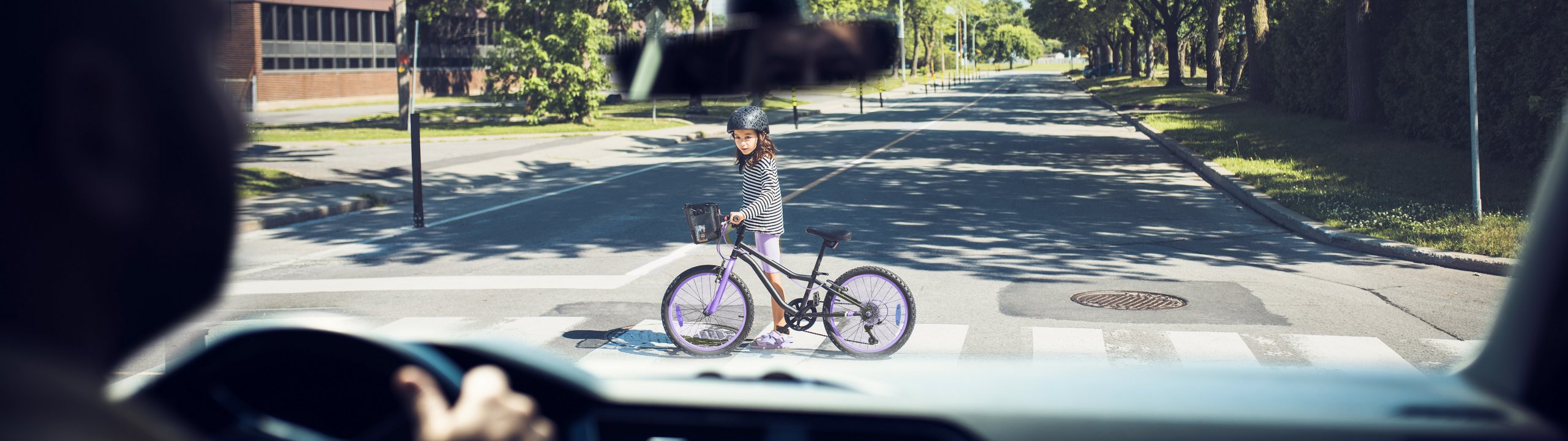 Kind überquert mit einem Fahrrad die Straße, gesehen aus einem Auto.