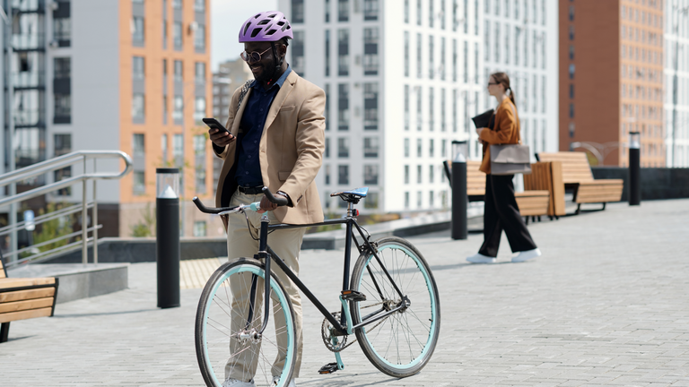 Mann mit Helm steht mit Fahrrad in der Stadt und schaut auf sein Smartphone.
