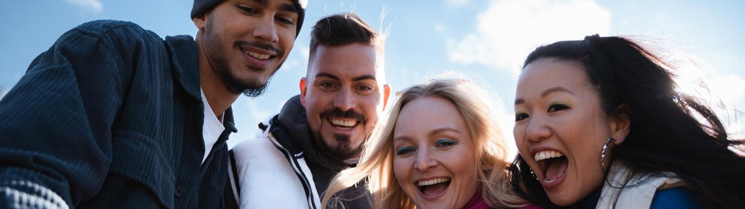 Vier junge Erwachsene lachen und machen gemeinsam ein Selfie im Freien.