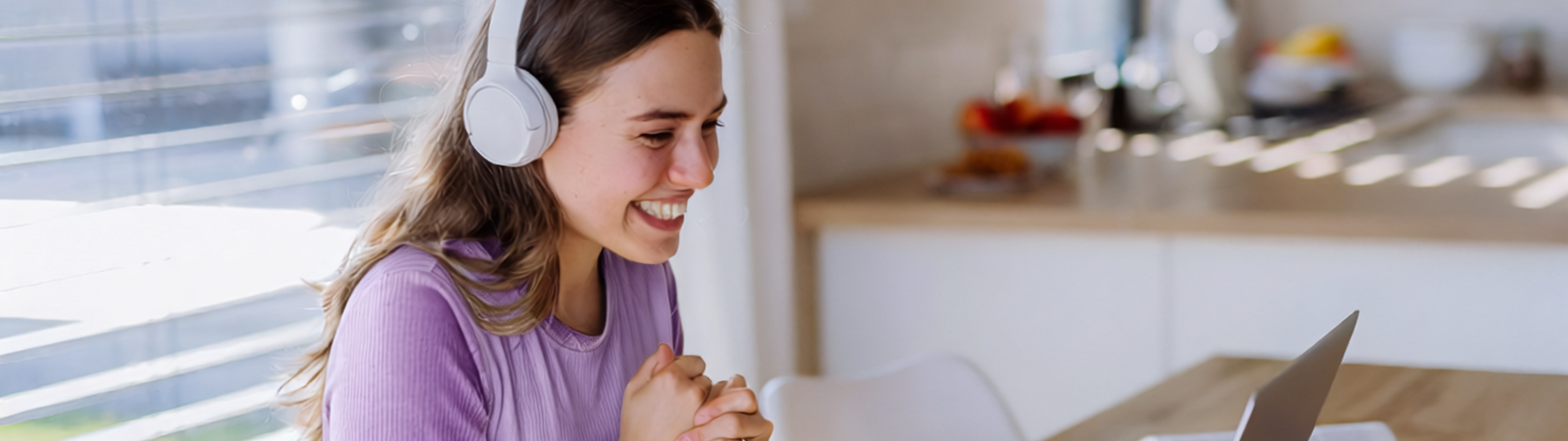 Eine junge Frau mit Kopfhörern lächelt vor ihrem Laptop bei einem Online-Meeting.