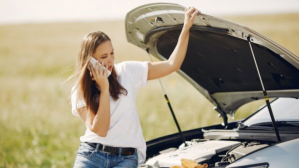 Frau steht mit Auto am Straßenrand und hat eine Panne