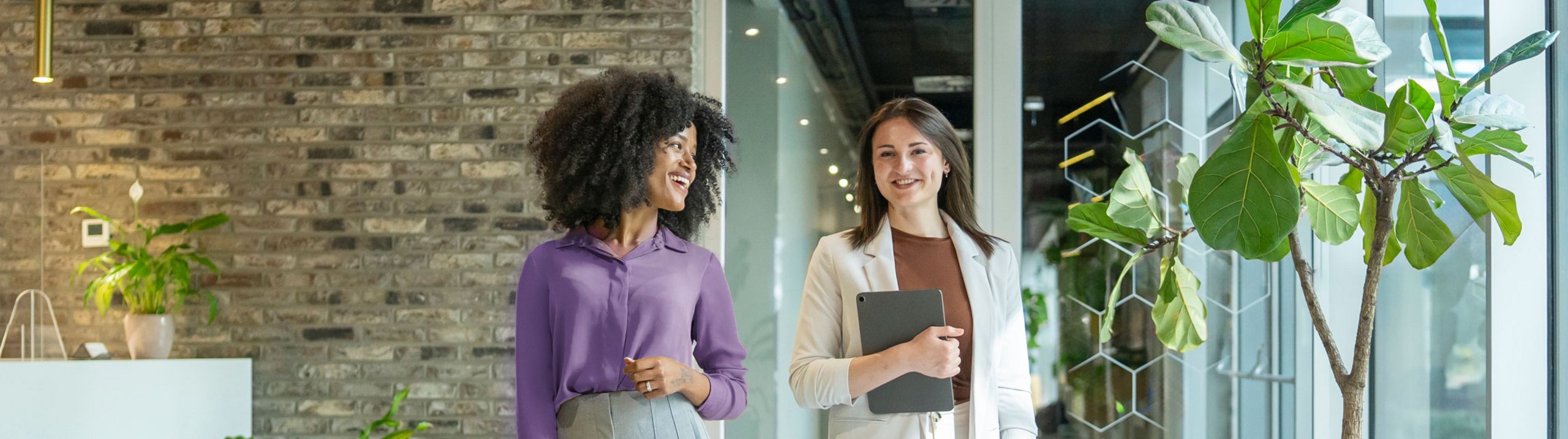 Zwei Frauen gehen gemeinsam durch ein modernes Bürogebäude und unterhalten sich.