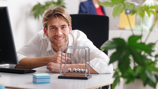 Nachhaltigkeit Mitarbeiter lächelnd am Arbeitsplatz mit Kugelpendel