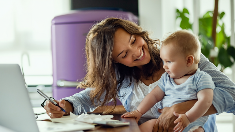 Eine Frau arbeitet am Laptop und hält ein Baby auf dem Arm