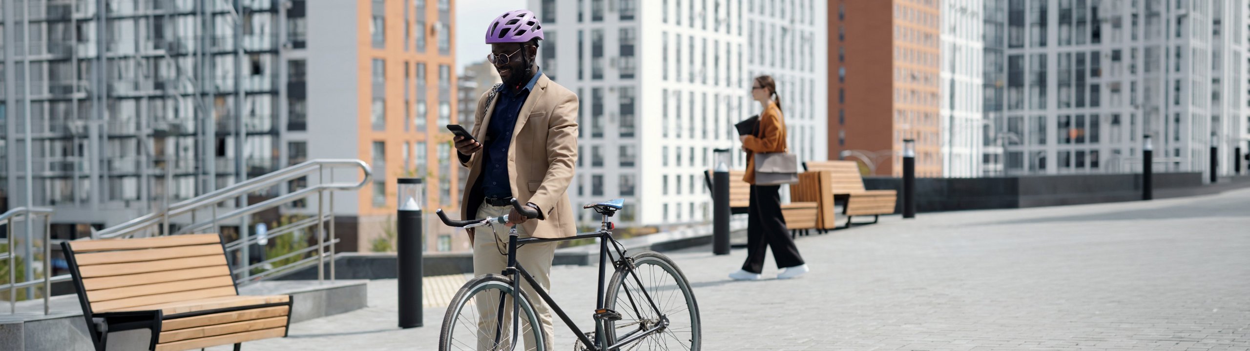 Mann mit Helm steht mit Fahrrad in der Stadt und schaut auf sein Smartphone.