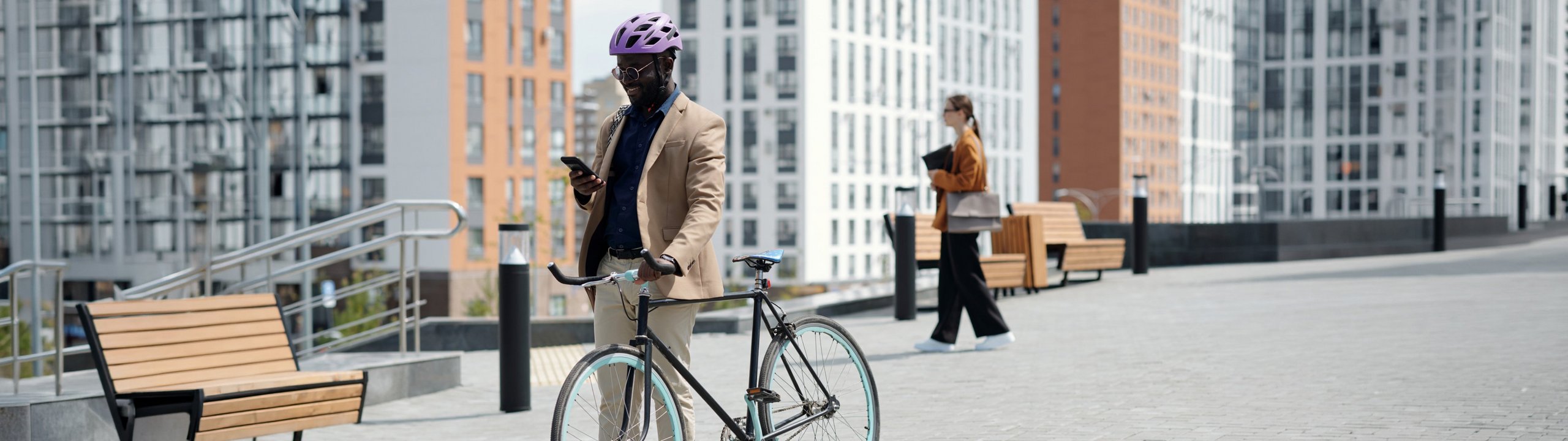 Mann mit Helm steht mit Fahrrad in der Stadt und schaut auf sein Smartphone.