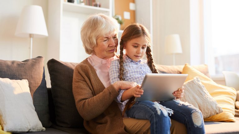 Großmutter und Kind sitzen auf dem Sofa und schauen gemeinsam auf ein Tablet.