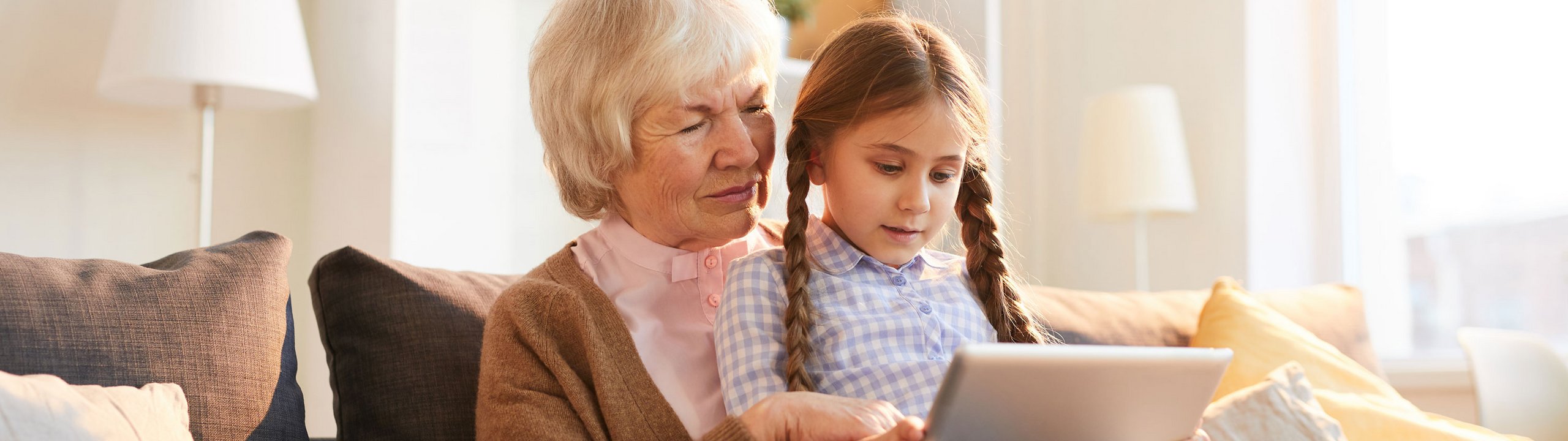 Großmutter und Kind sitzen auf dem Sofa und schauen gemeinsam auf ein Tablet.