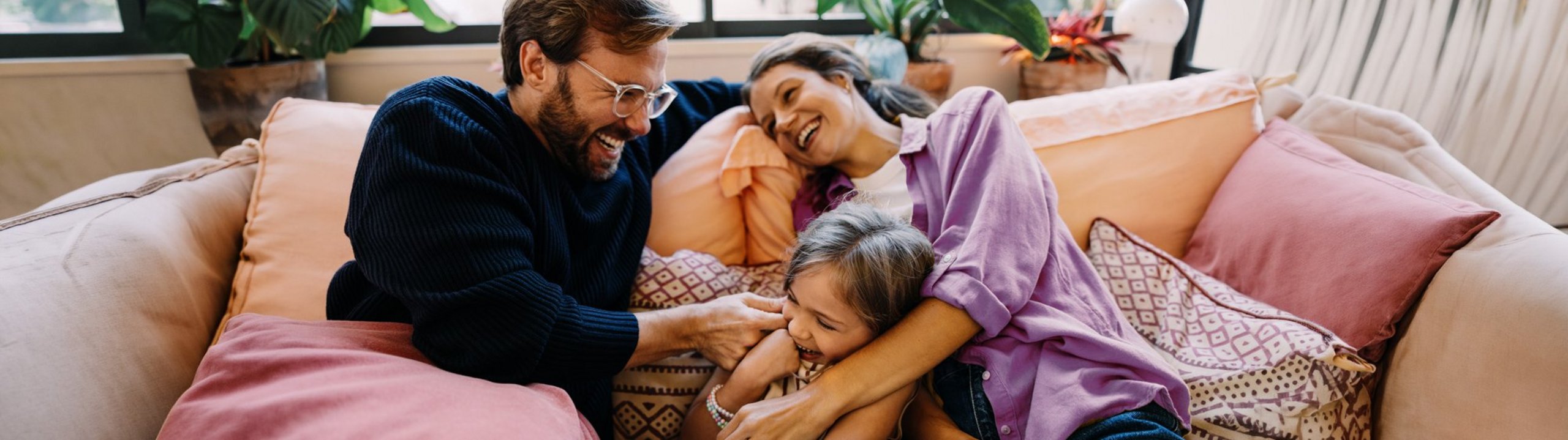 Familie kuschelt lachend auf dem Sofa.