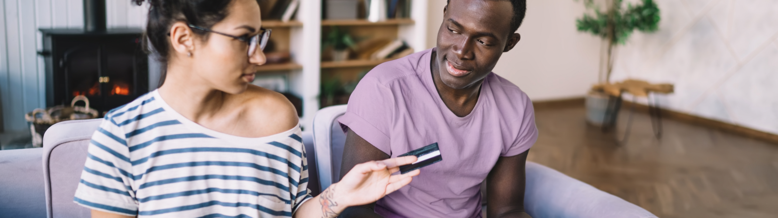 Zwei Personen sitzen auf dem Sofa und schauen gemeinsam auf eine Kreditkarte und Unterlagen.
