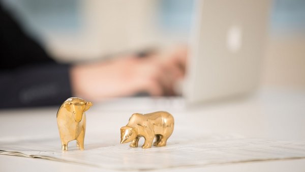 Ein goldener Stier und Bär stehen vor einem Laptop auf einem Schreibtisch