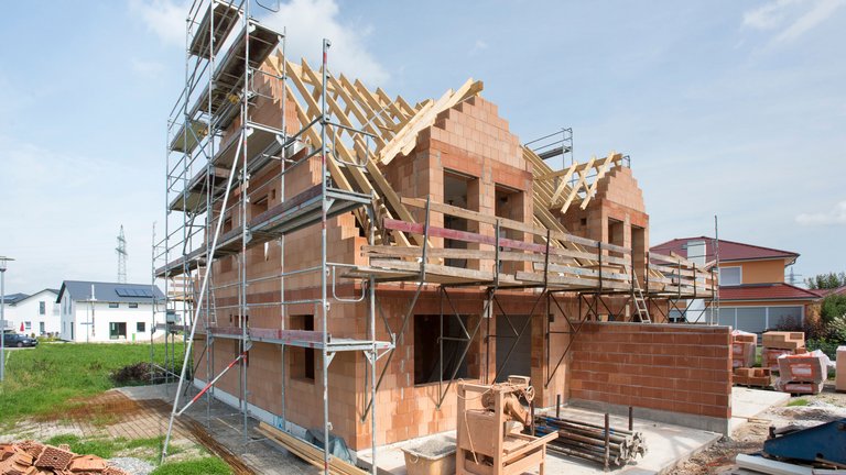 Rohbau eines Hauses mit Gerüst und Dachkonstruktion auf einer Baustelle.