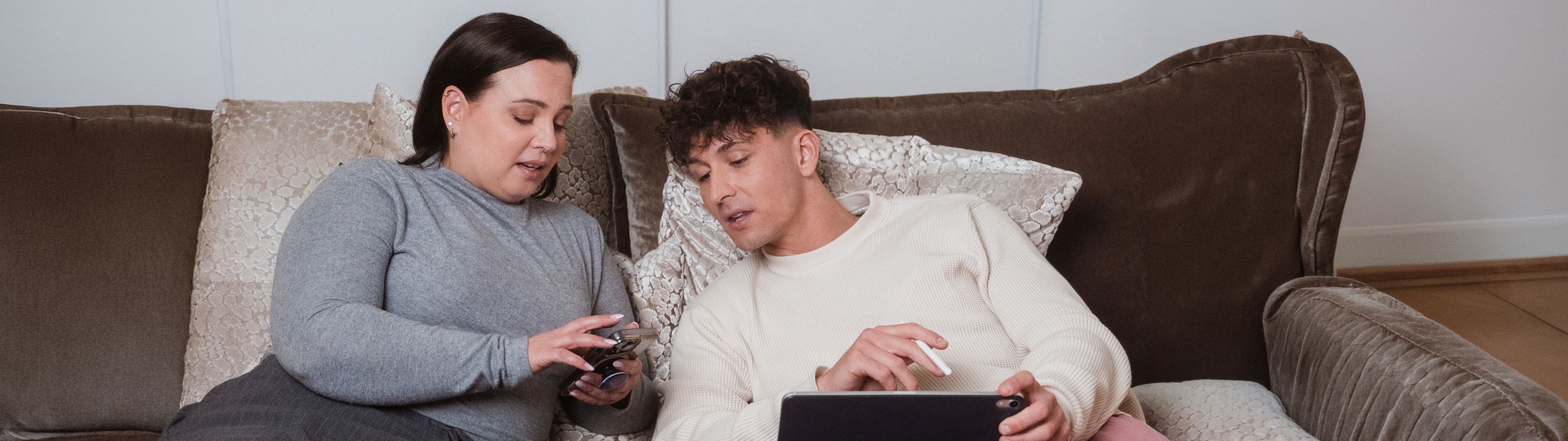 Zwei Personen vergleichen auf dem Sofa Informationen auf Smartphone und Tablet.