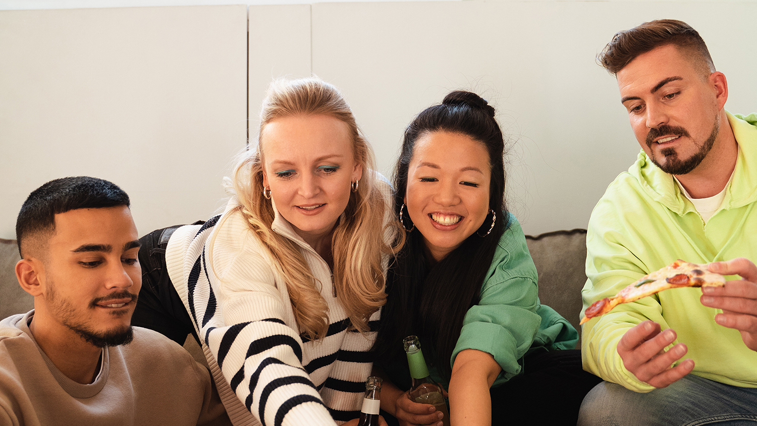 Wie funktioniert eine WG? Vier junge Menschen sitzen zusammen auf einer Couch und lachen