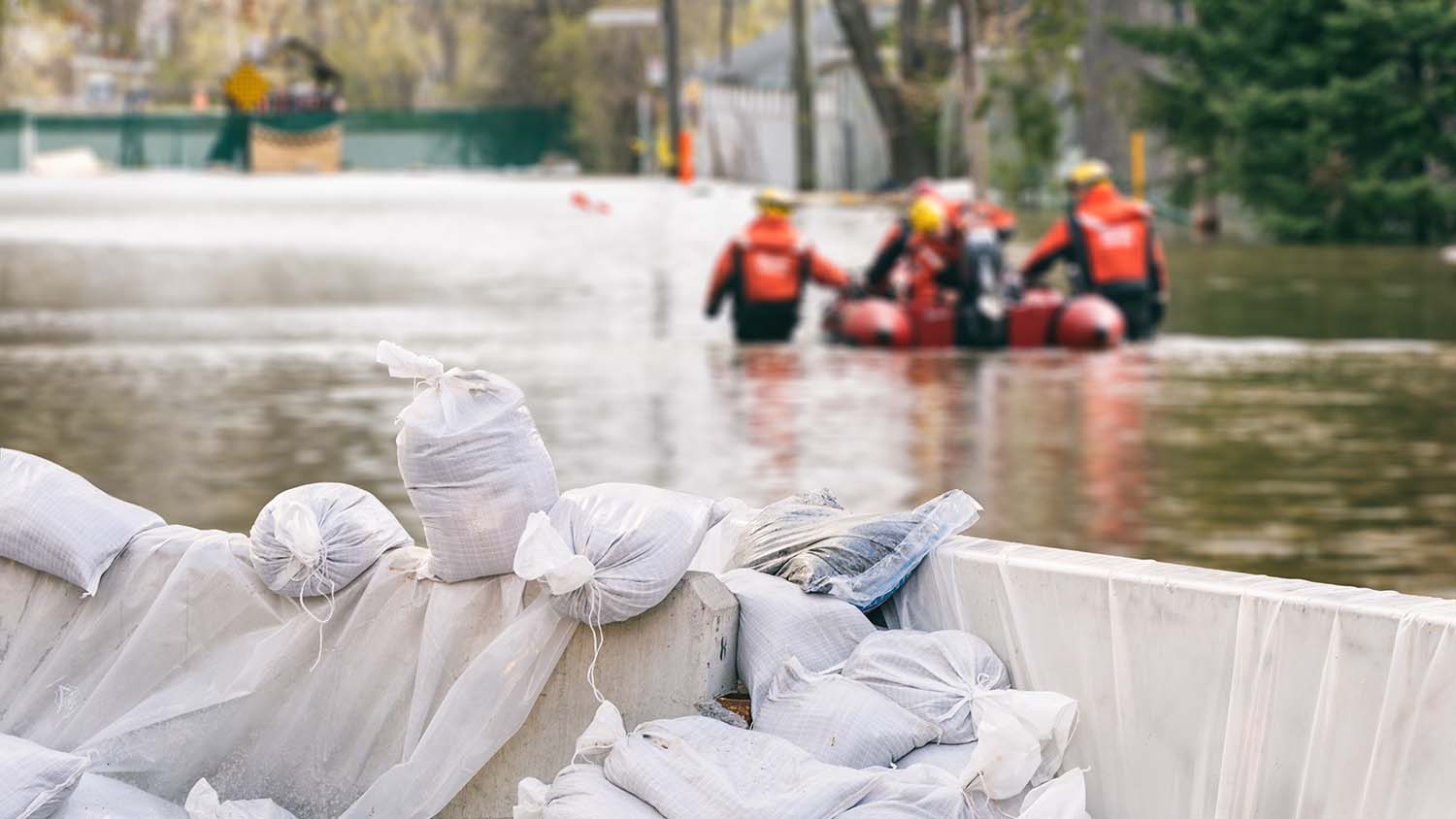 Sandsäcke mit überfluteten Häusern und einem Rettungsteam im Hintergrund