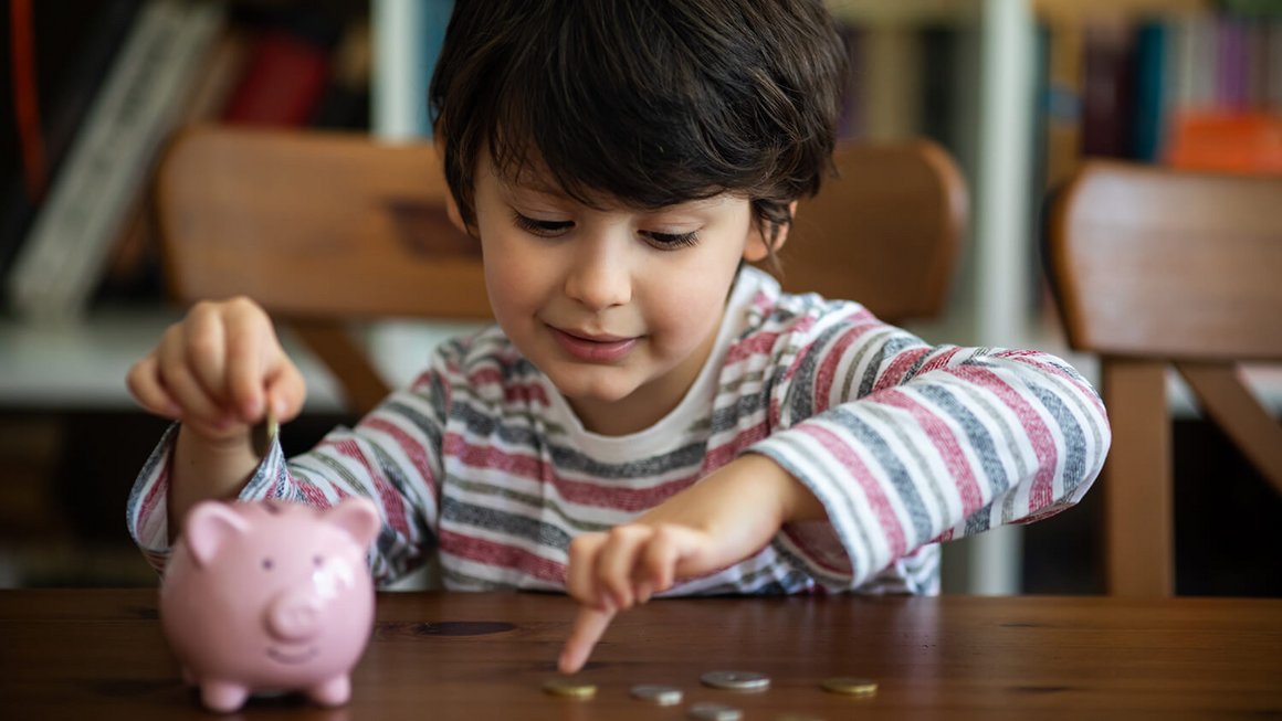 Kind mit Sparschwein und Geldmünzen – monatliche Fixkosten im Haushalt