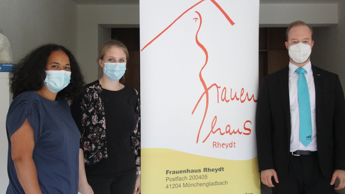 Zwei Frauen und ein Mann stehen mit Maske aufgereiht. In der Mitte ist ein Banner für die Spendensammelaktion des Frauenhaus in Mönchengladbach Rheydt