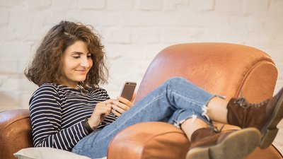 Junge Frau glücklich auf einem Sessel mit Handy OVB
