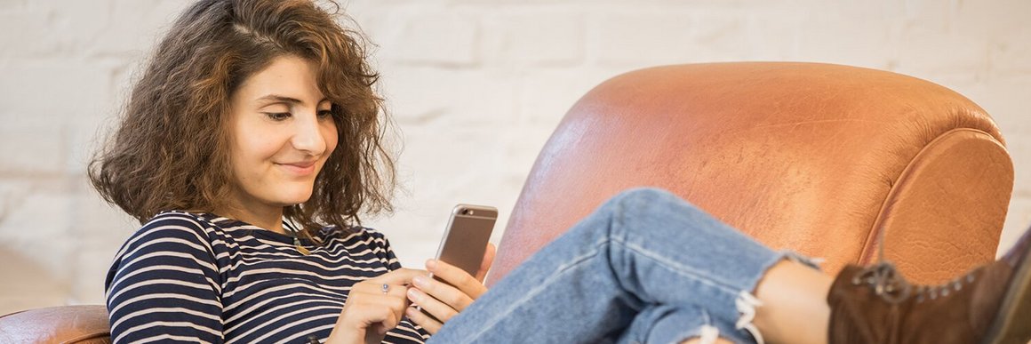 Junge Frau glücklich auf einem Sessel mit Handy OVB