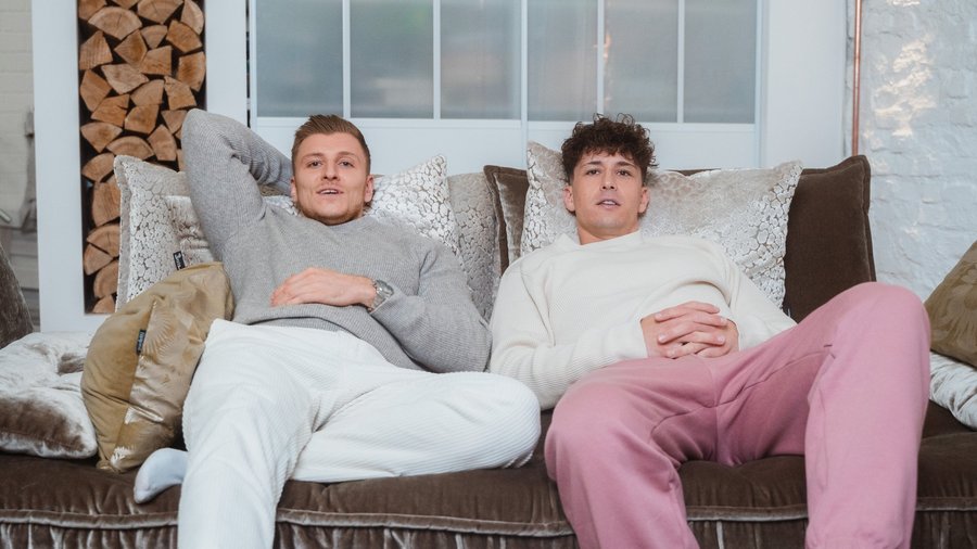 Zwei junge Männer sitzen auf einer Couch.