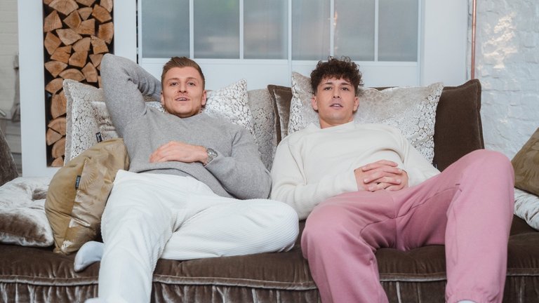 Zwei junge Männer sitzen gemeinsam auf einer Couch.