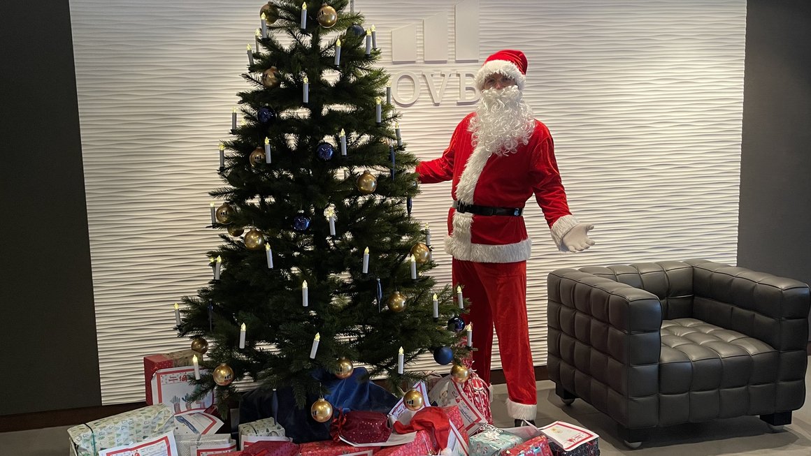 Weihnachtsmann in OVB Zentrale am Heumarkt steht vor Weihnachtsbaum, vor dem viele Geschenke liegen
