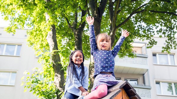 Zwei Mädchen sitzen auf Spielhaus eines Spielplatz und freuen sich im Sommerwetter