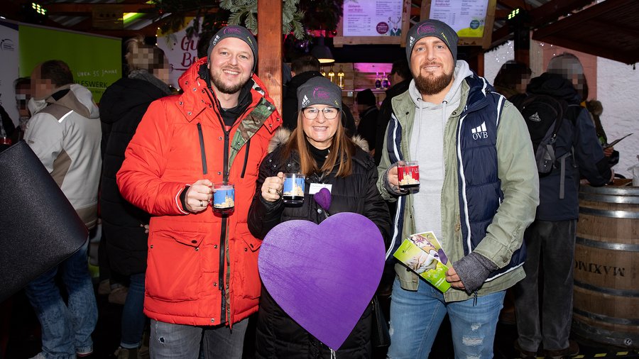 Zwei Männer und eine Frau in der Mitte trinken Glühwein für guten Zweck