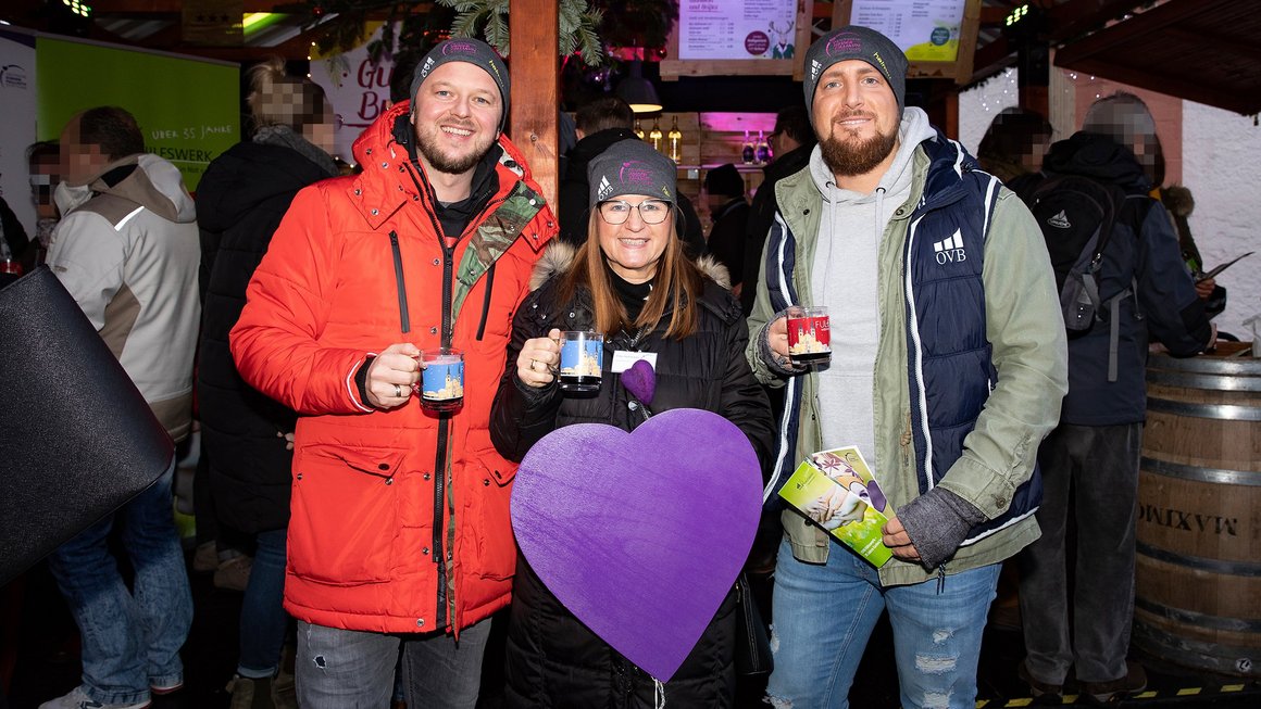 Zwei Männer und eine Frau in der Mitte trinken Glühwein für guten Zweck