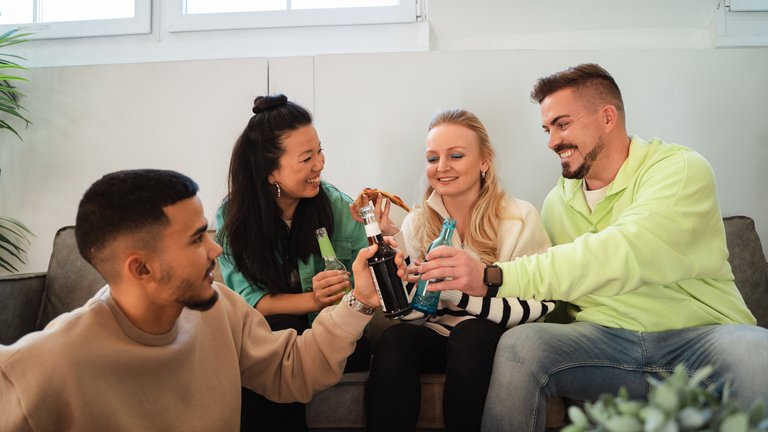 Vier junge Menschen sitzen zusammen auf einer Couch und genießen Snacks und Softdrinks.