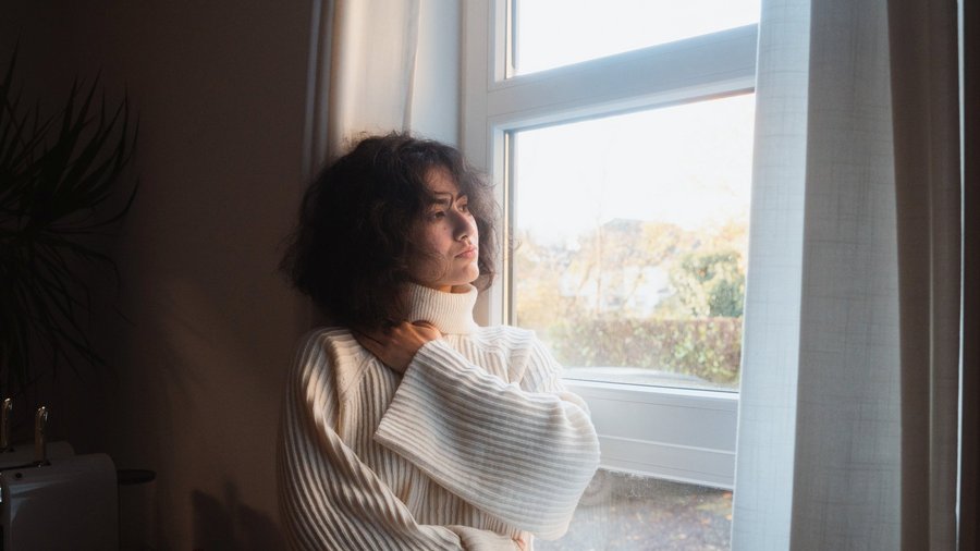 Frau blickt nachdenklich aus dem Fenster.