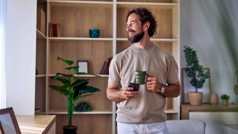 Junger Mann mit Tasse Kaffee in der Hand schaut aus dem Fenster