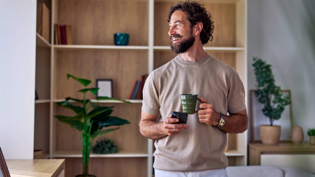 Junger Mann mit Tasse Kaffee in der Hand schaut aus dem Fenster