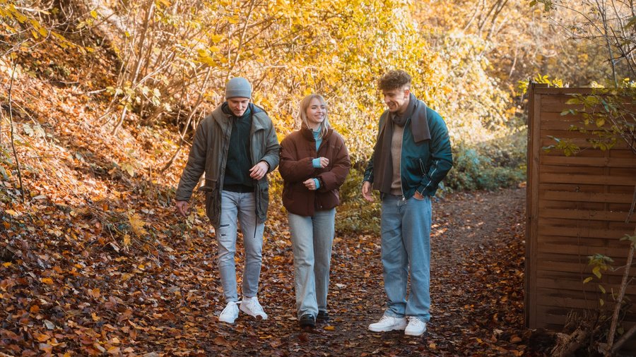 Gruppe von drei jungen Leuten spaziert gelassen an einem Herbst-Tag.