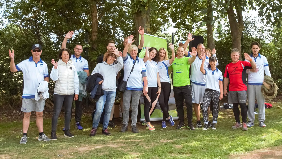 Eine Vielzahl Männer und Frauen bei der OVB Hilfswerk Family and Friends Aktion stehen auf dem Rasen, tragen weisse Leibchen und winken freundlich