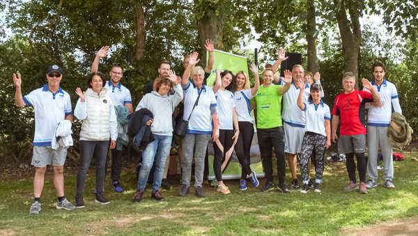 Eine Vielzahl Männer und Frauen bei der OVB Hilfswerk Family and Friends Aktion stehen auf dem Rasen, tragen weisse Leibchen und winken freundlich