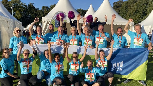 OVB Mitarbeiter beim B2Run in Köln halten einen Banner hoch und winken. Es ist Sommer und sehr warm