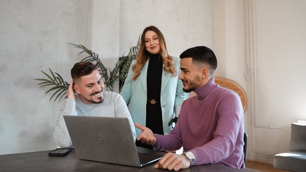 zwei Männer und eine Frau sitzen vor dem Laptop