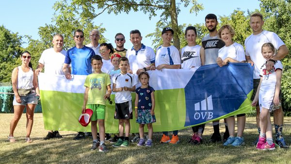 OVB Mitarbeiter stehen mit ihren Kindern im Sommer auf einer Wiese und halten einen grün weissen OVB Banner hoch