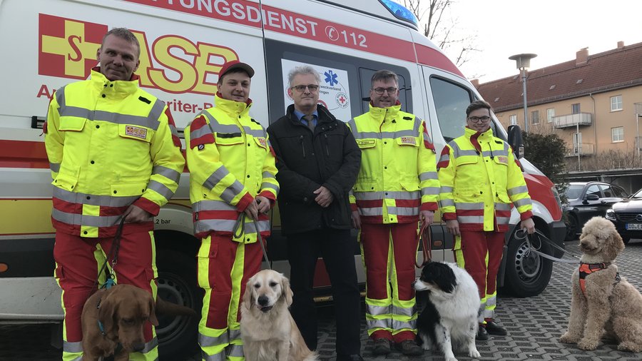 Rettungshunde und Sanitäter des Arbeiter-Samariter-Bunds (ASB) Regionalverbandes Ostthüringen e.V. stehen vor Rettungswagen