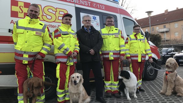 Rettungshunde und Sanitäter des Arbeiter-Samariter-Bunds (ASB) Regionalverbandes Ostthüringen e.V. stehen vor Rettungswagen
