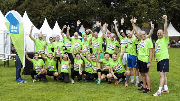 23 Männer und Frauen der OVB stehen auf einer Wiese im Sommer. Sie tragen grüne Trikots und recken die Fäuste siegesgewiss in die Luft beim B2 Run