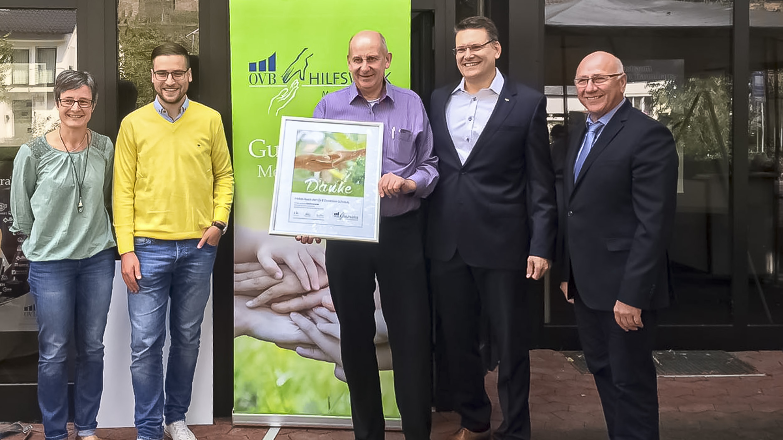 OVB Ahrtal Bezirksdirektor Wolfgang Schröck übergibt Spende an Mitarbeiter des Hospitz im Artal vor dem Gebäude
