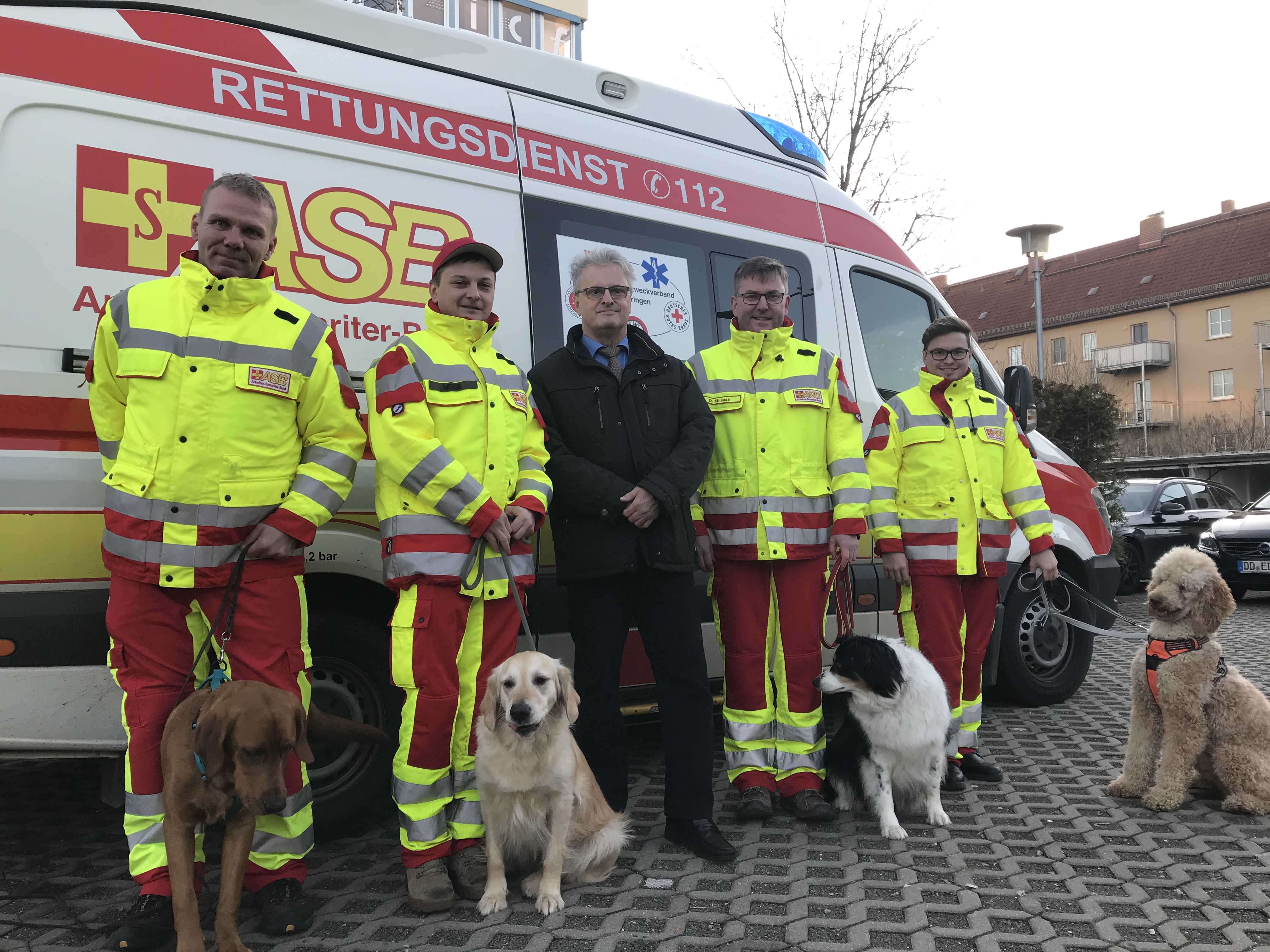Rettungshunde und Sanitäter des Arbeiter-Samariter-Bunds (ASB) Regionalverbandes Ostthüringen e.V. stehen vor Rettungswagen