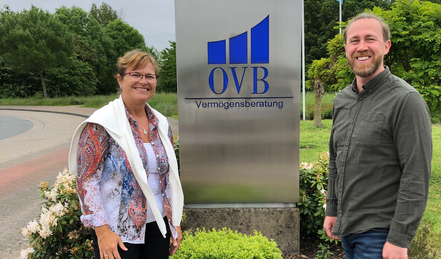 OVB Schild in der Mitte. Frau links mit Brille, Mann rechts mit Bart