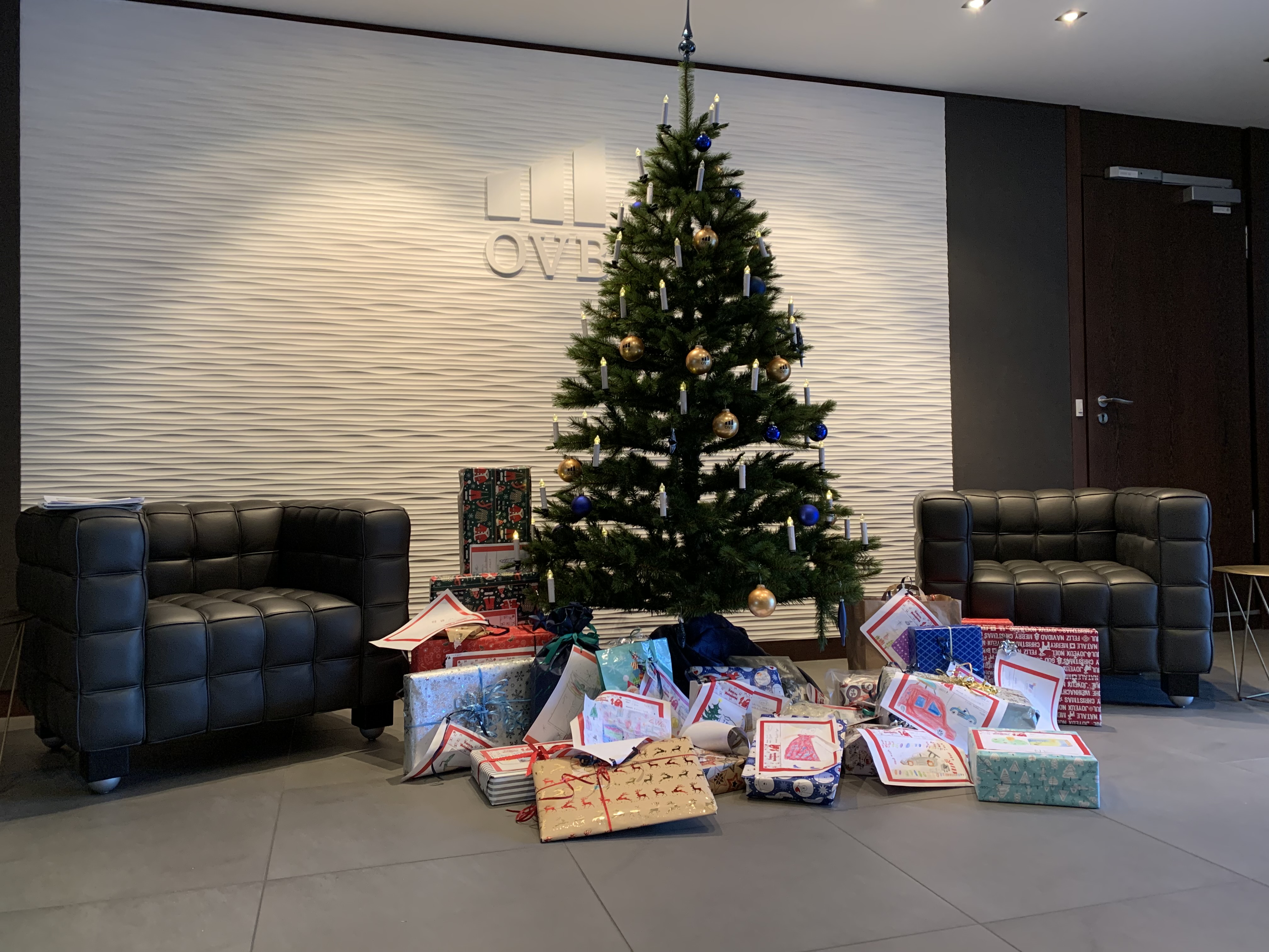 Geschmückter Weihnachtsbaum im Foyer der OVB Zentrale am Kölner Heumarkt. Vor dem Weihnachtsbaum liegen viele eingepackte Geschenke